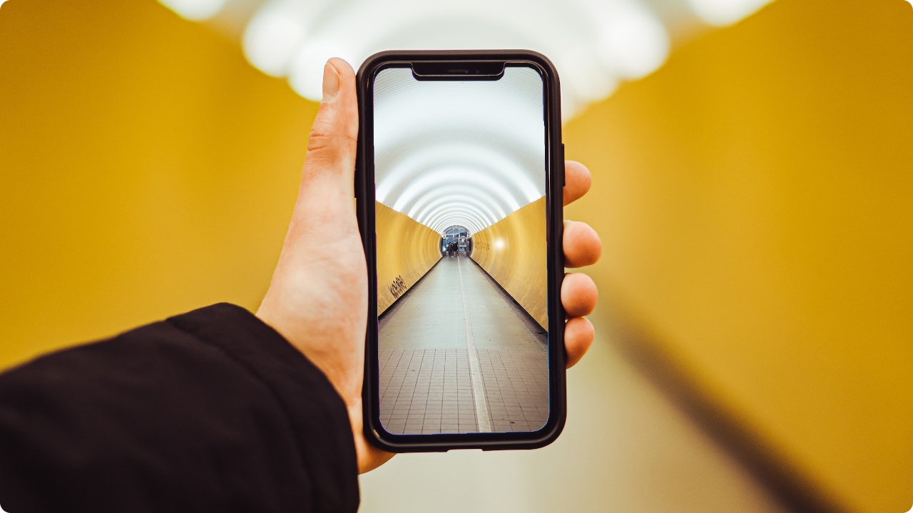 A person holding a phone up to take a picture of a rounded hallway.